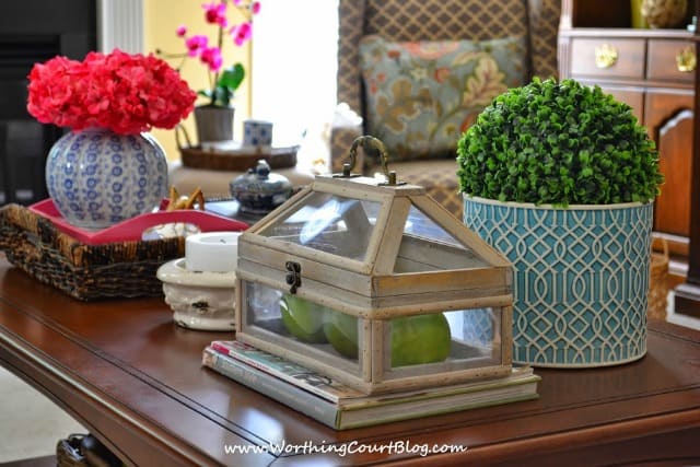 A glass terrarium is beside a boxwood plant on the table.