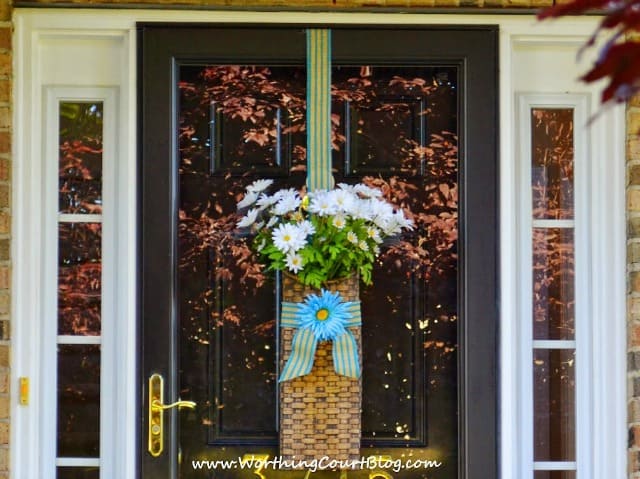 A front door with windows and a basket full of daisies.