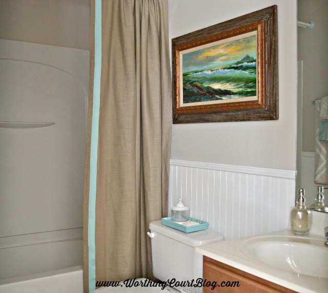 Use a drapery panel for a shower curtain. Hang a clear plastic shower curtain on a separate rod on the backside to protect it while showering. Use iron on tape to add a border of ribbon to the edge of the panel. 