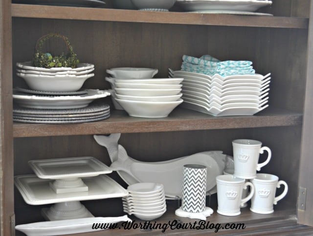 Gray and white stacked dishes and accessories in a kitchen display cabinet