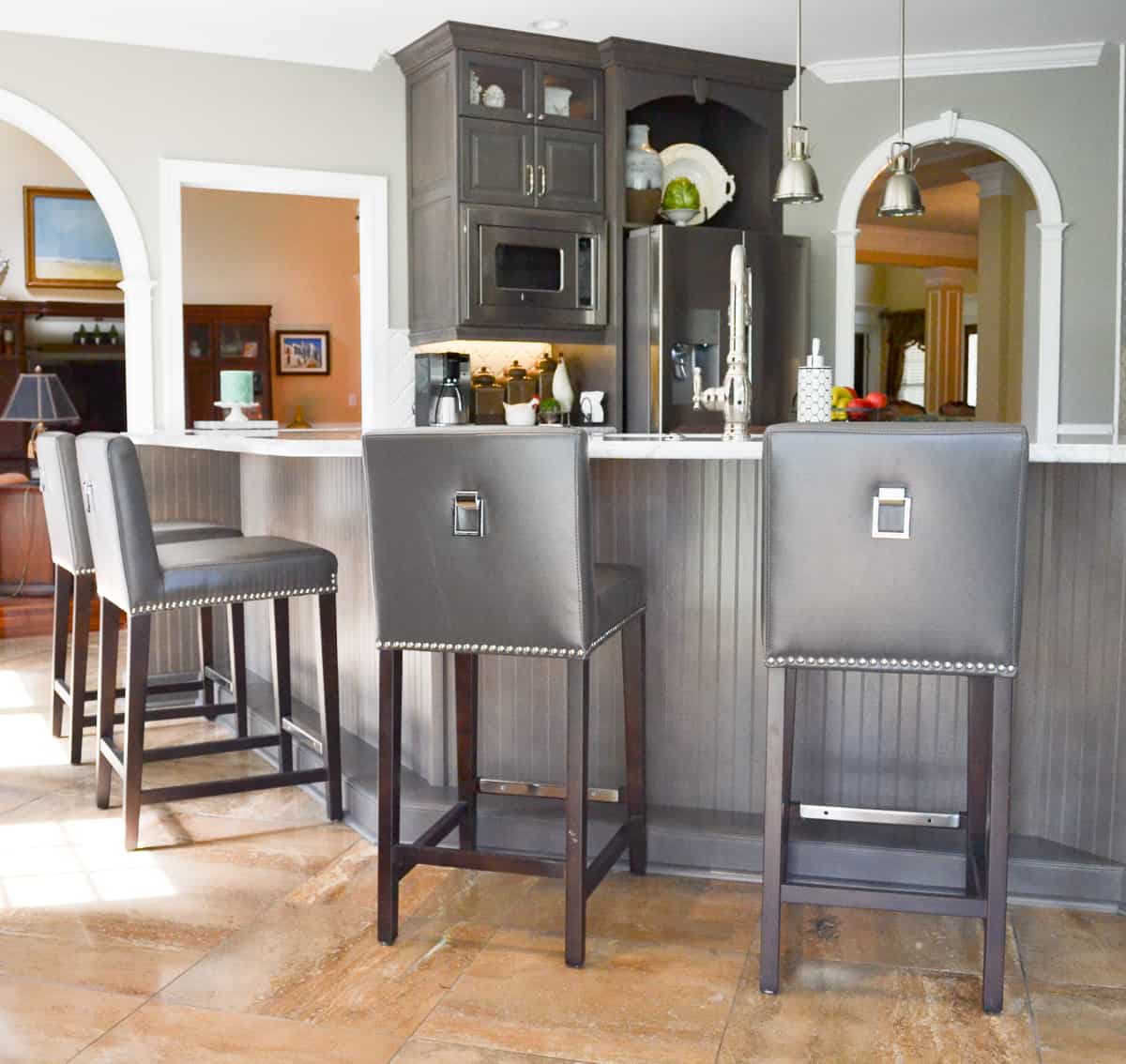 front of gray kitchen island covered with beadboard paneling and gray leather barstools