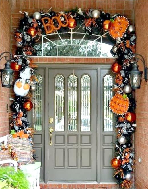 The door to this home has Halloween decor in orange, gold all around it with the words BOO in an orange sign.