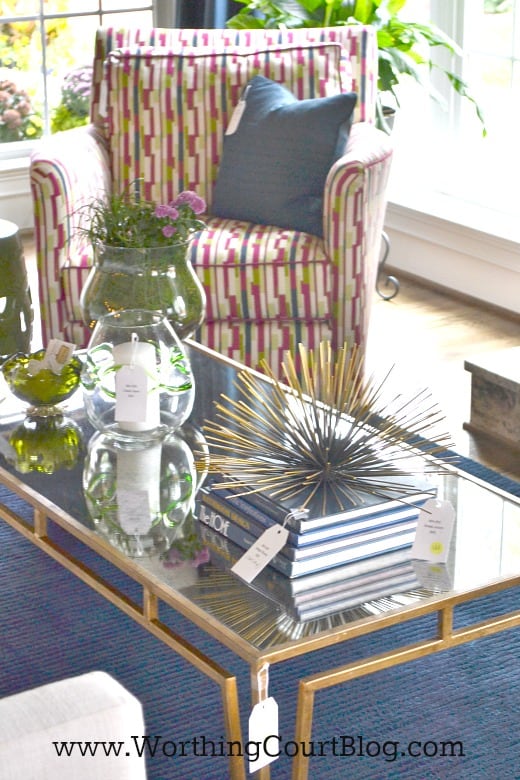 A glass and brass coffee table with books and vases on it.