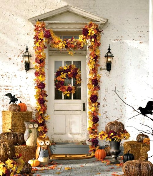 Autumn leaves surround the door frame of this house in gold and purple, plus pumpkins and bales of hay out front. There are also black crows.