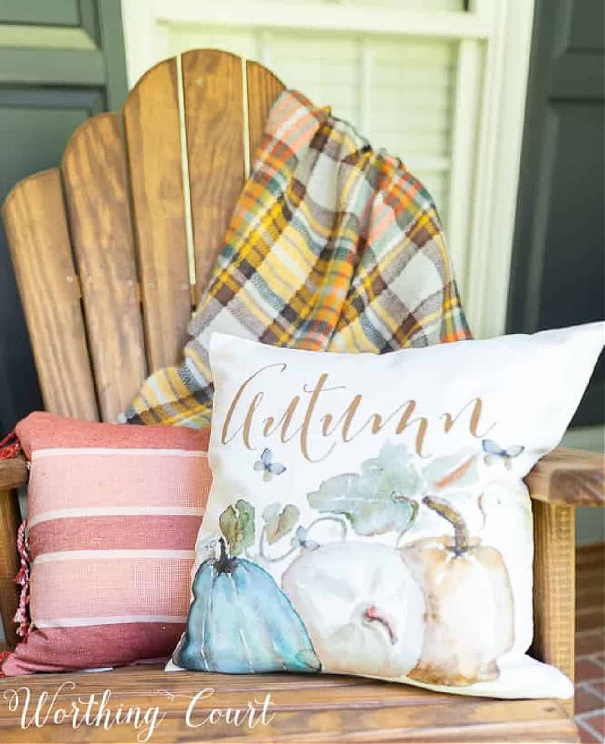natural wood chair on a porch with fall throw pillows and a plaid fall throw blanket over the back