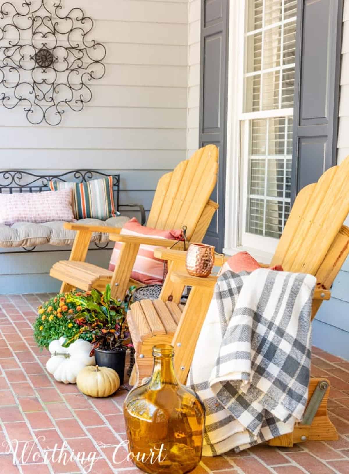 pair of natural wood gliders on front porch with fall decorations and a plaid throw blanket