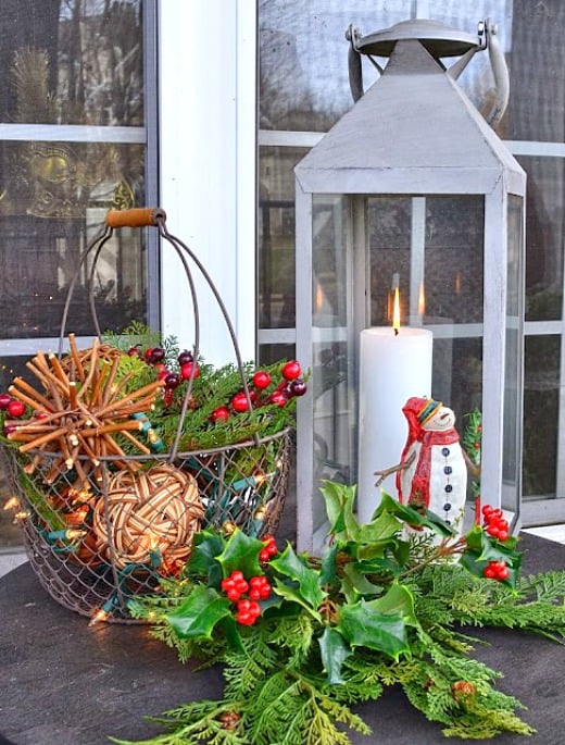 Chrismtas vignette outside with a small snowman and a metal basket filled with greenery.