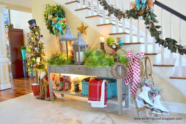 A foyer beautifully decorated for Christmas with a decorated planter, a wreath on the wall, bows and a garland on the staircase.