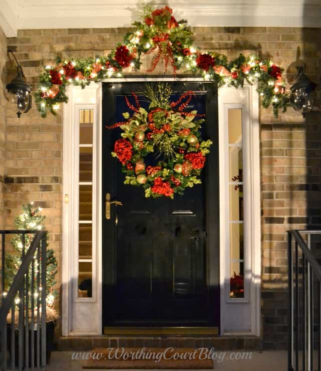 Front porch decorated for Christmas with a large wreath on the front door.