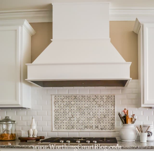 The white kitchen with a white range hood and the backsplash.