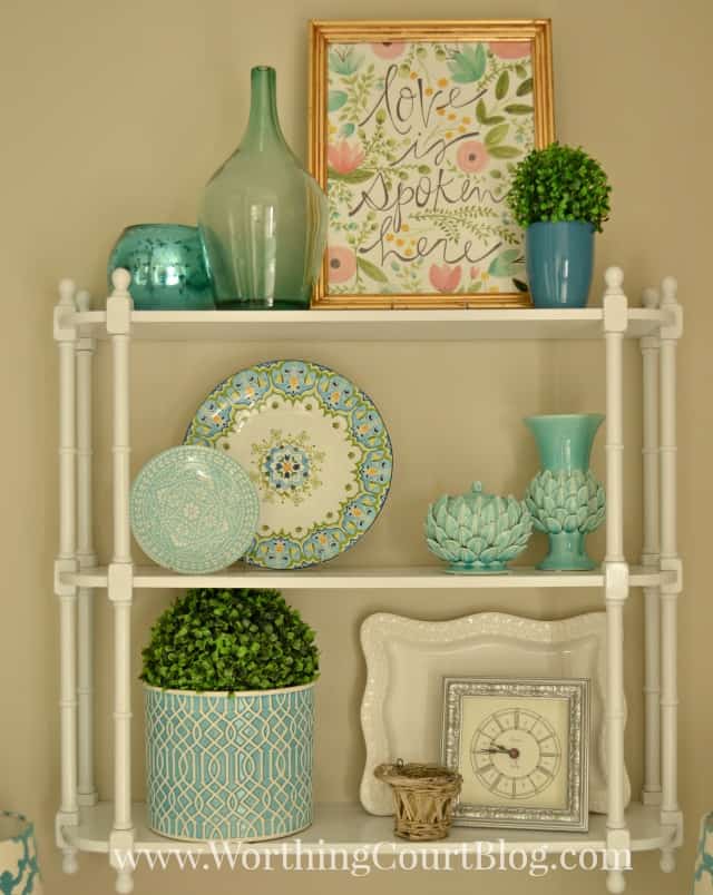 There is blue clear glass, decorative plates and vases on the white shelf.