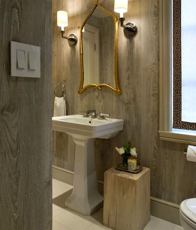 Faux bois wallpaper in the bathroom with an ornate gold mirror.