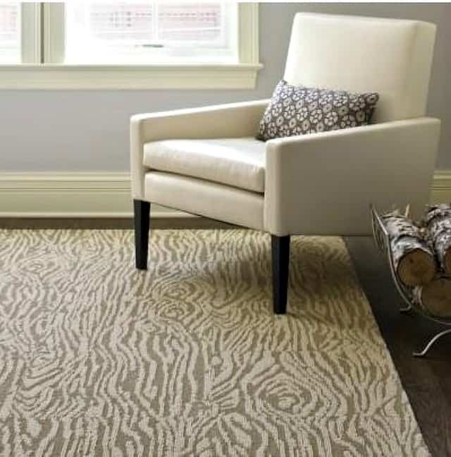 Faux bois area rug with a neutral armchair and throw pillow on it.