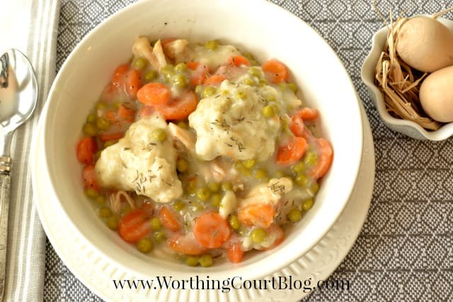 The bowl of stew on the table with a silver spoon beside it.