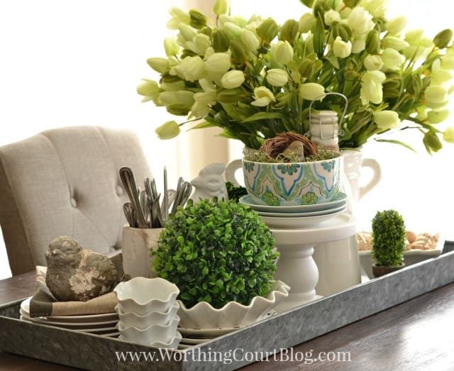 Tulips in a white pitcher beside greenery and small bird figurine.