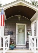 front porch with a white door, gray shingles and an arched ceiling