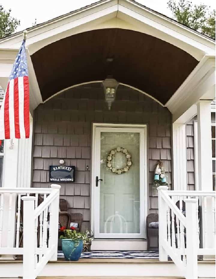 front porch with a white door, gray shingles and an arched ceiling