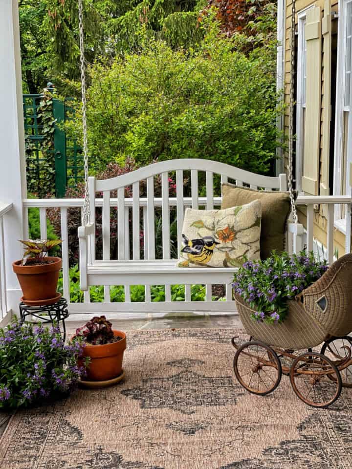 white porch swing and a vintage baby buggy filled with greenery on a front porch