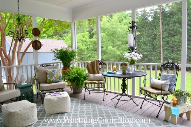 There is large trees and grass outside of the porch area.