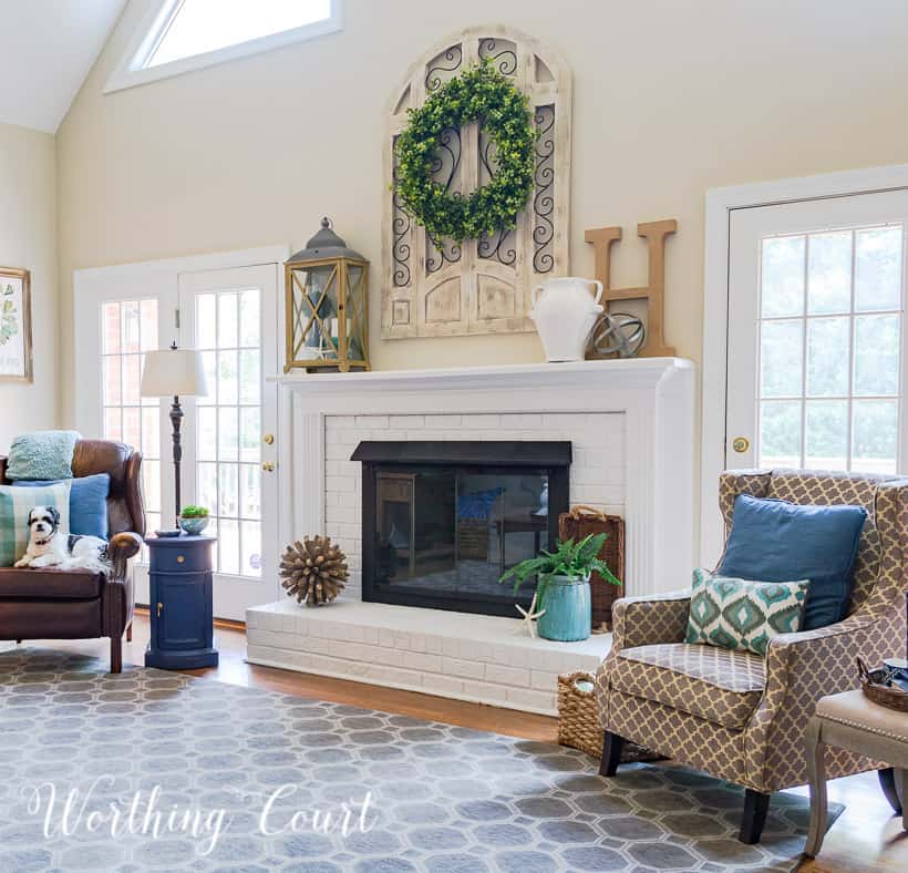 The panted white fireplace with a large green wreath above it.