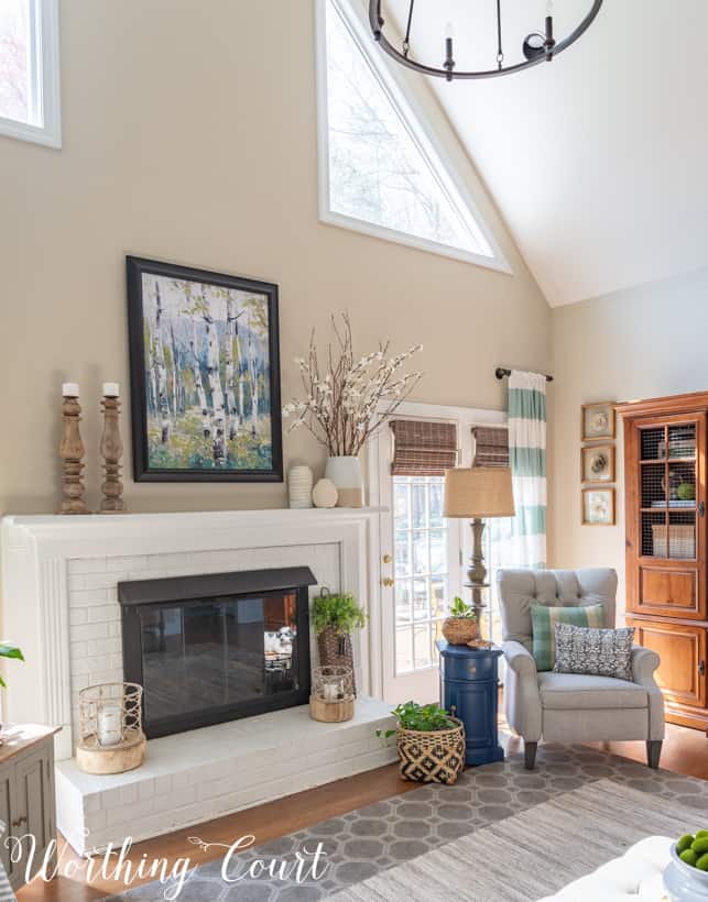 There is a forest watercolour picture above the fireplace beside the candle sticks.