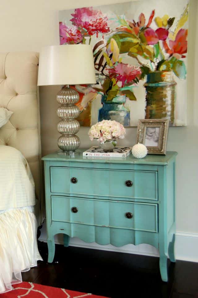 A turquoise nightstand beside a white bed.