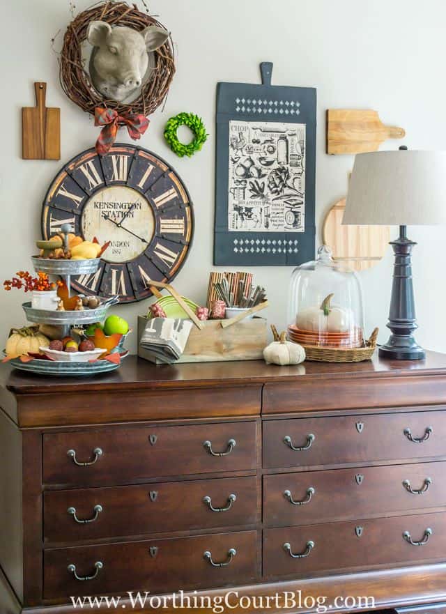 A wooden sideboard with a galvanized treat tray full of pumpkins and gourds.   There is a cloche with a white pumpkin in it.