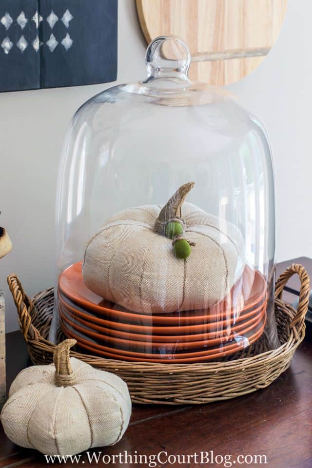 A white fabric pumpkin with acorns around the stem under the cloche.