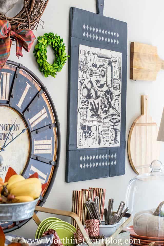 A wall above the sideboard with cutting boards that are decorative hanging beside Hubert the pig.