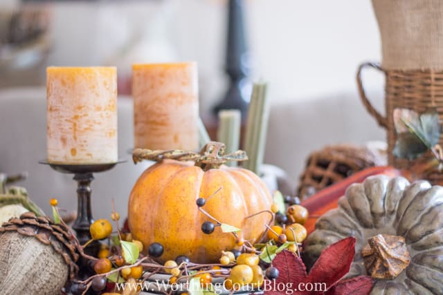 A pumpkin is sitting by the amber candles on the table.