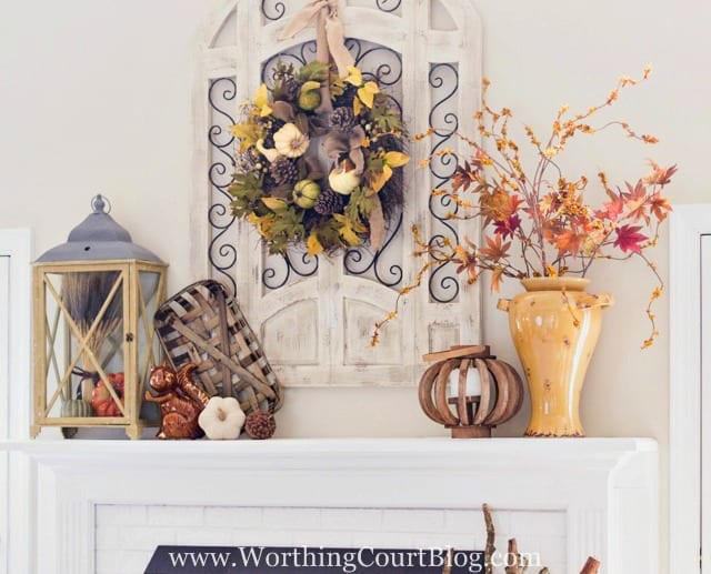 There is an urn filled with fall leaves and also a lantern on the fireplace mantel.