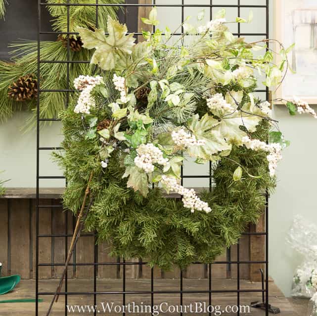A wreath on a stand being decorated with leaves and white berries.