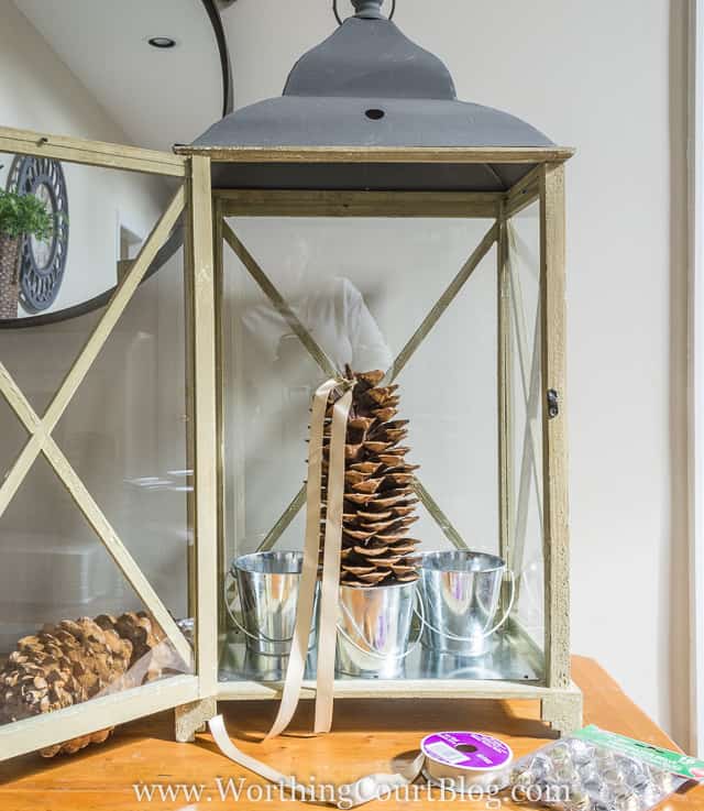 A pine cone on a silver bucket with a gold ribbon tied around the top of it.