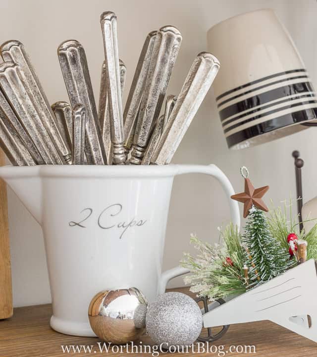 knives are in a white pitcher with silver ornaments beside it.