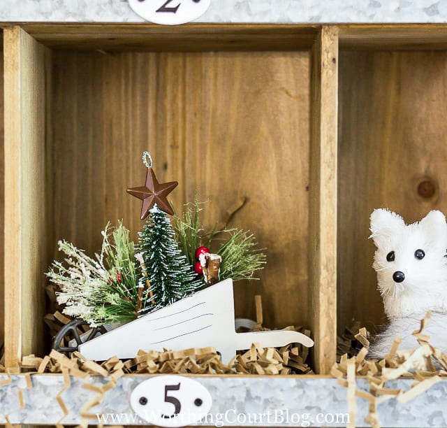 There is a wheelbarrow in a cubby holding a Christmas tree and faux greenery.