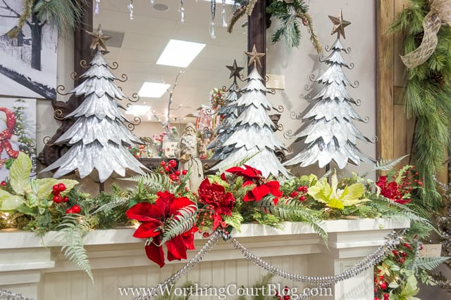 Decorative Christmas trees on the mantel plus red flowers and berries.