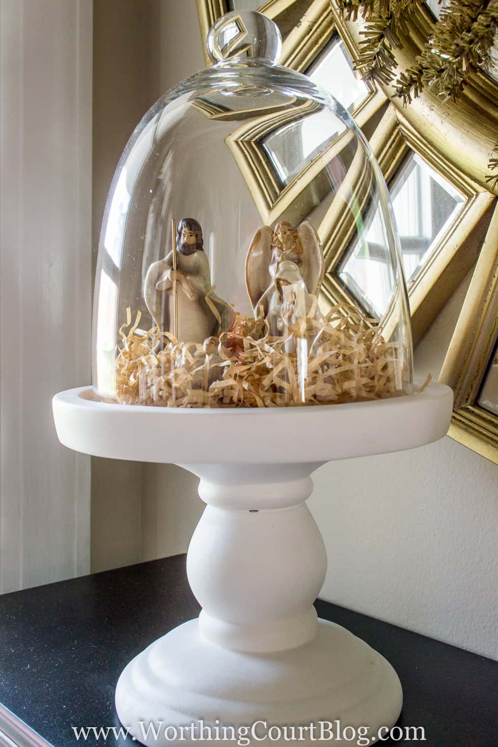 A tiny nativity set is very simply displayed under a glass cloche.