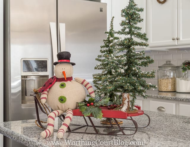 A snowman figurine is on a sleigh with mini trees.