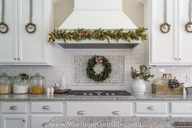 Little wreaths are hanging on the white kitchen cabinets.