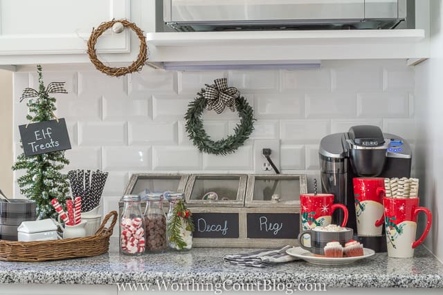 The Keurig coffee maker is in the corner with a mini tree with Elf treats, and holiday cups beside it.