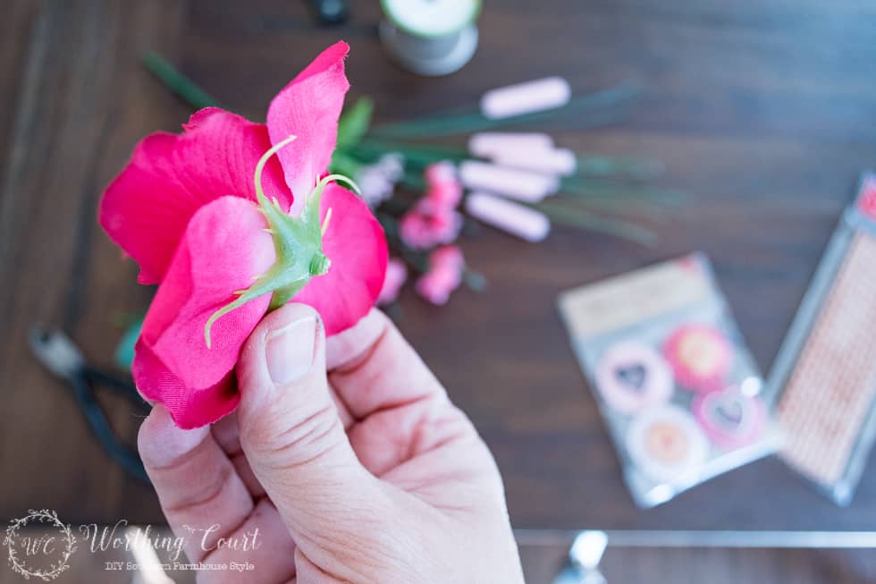 Holding the pink flowers between two fingers.