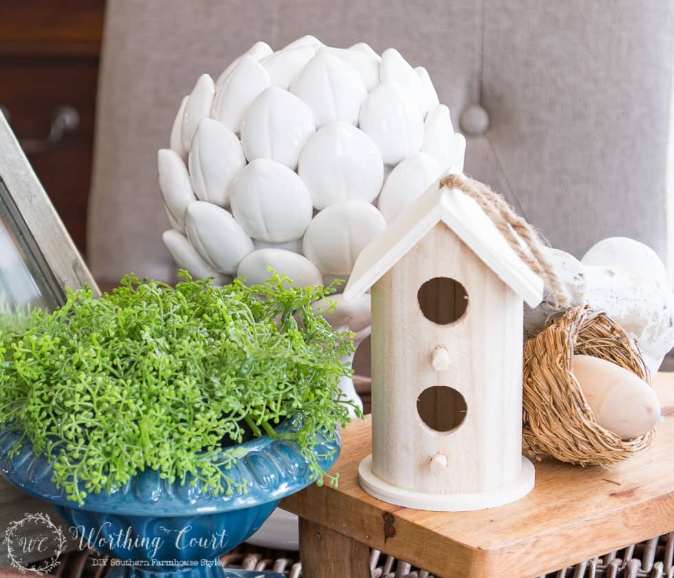 A wooden birdhouse beside a blue pot filled with greenery.