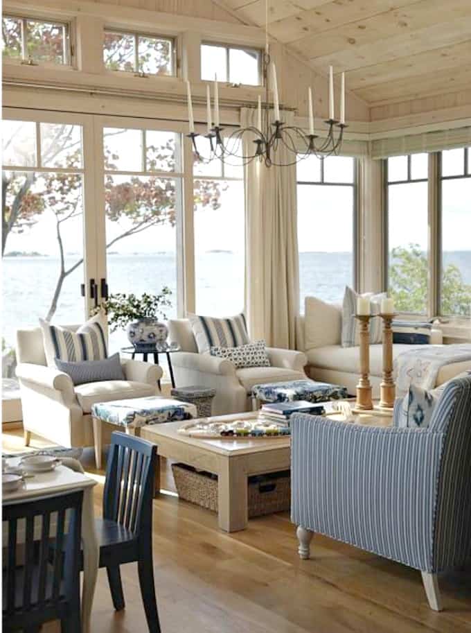 A living room with floor to ceiling windows overlooking the water and blue striped couches and pillows.