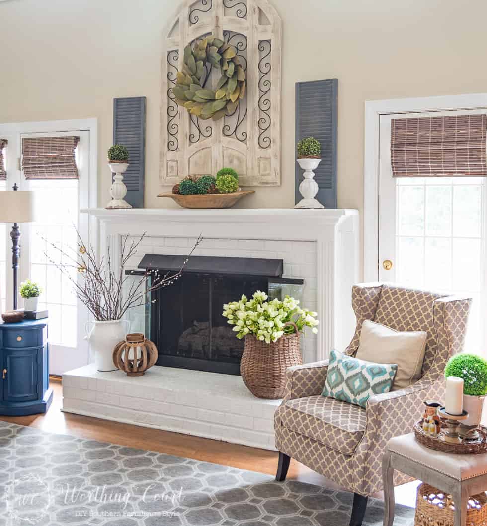 This fireplace celebrates the arrival of spring by filling the mantel and hearth with texture and a mix of real and faux branches and greenery. From a basket overflowing with tulips to an urn filled with pussy willow branches, to a magnolia leaf wreath to an abundance of boxwood orbs, there's no doubt what season it is in this family room.