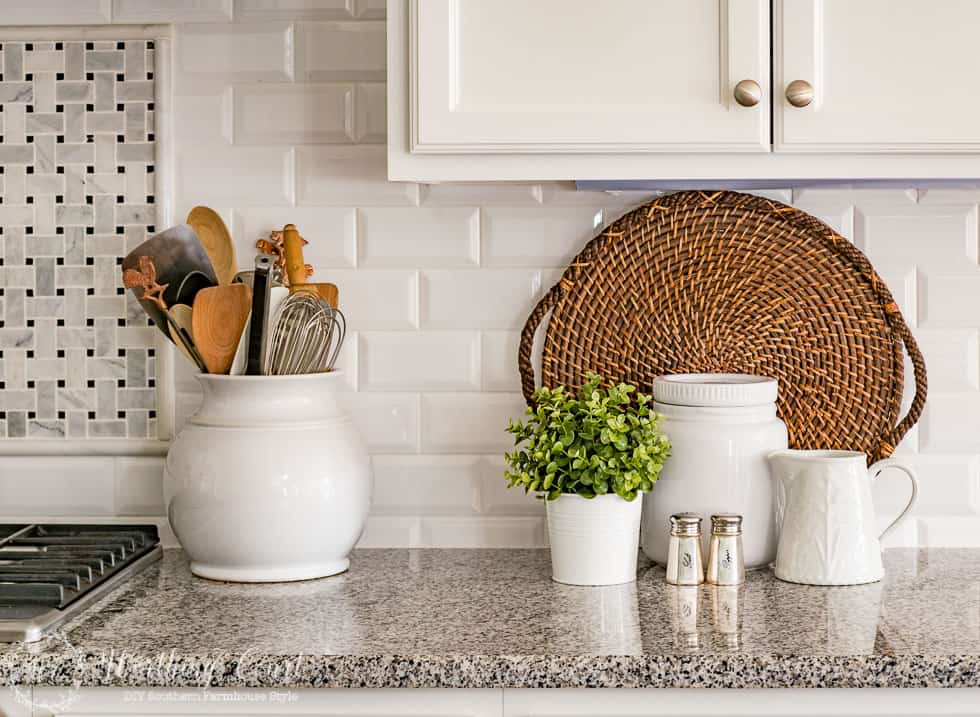 There is a woven serving tray against the white backsplash in the kitchen.