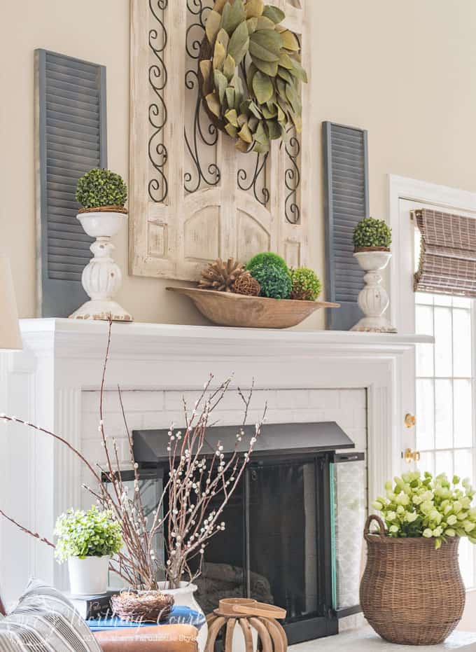 There is a wooden dough bowl and tulips by the fireplace.