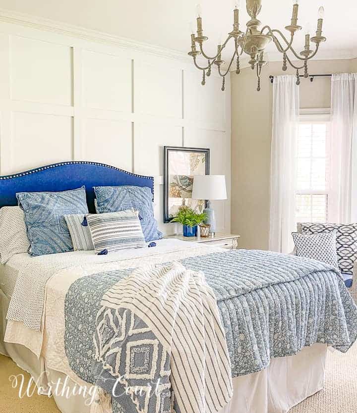 bed with a blue upholstered headboard and blue and white bedding against a white board and batten wall