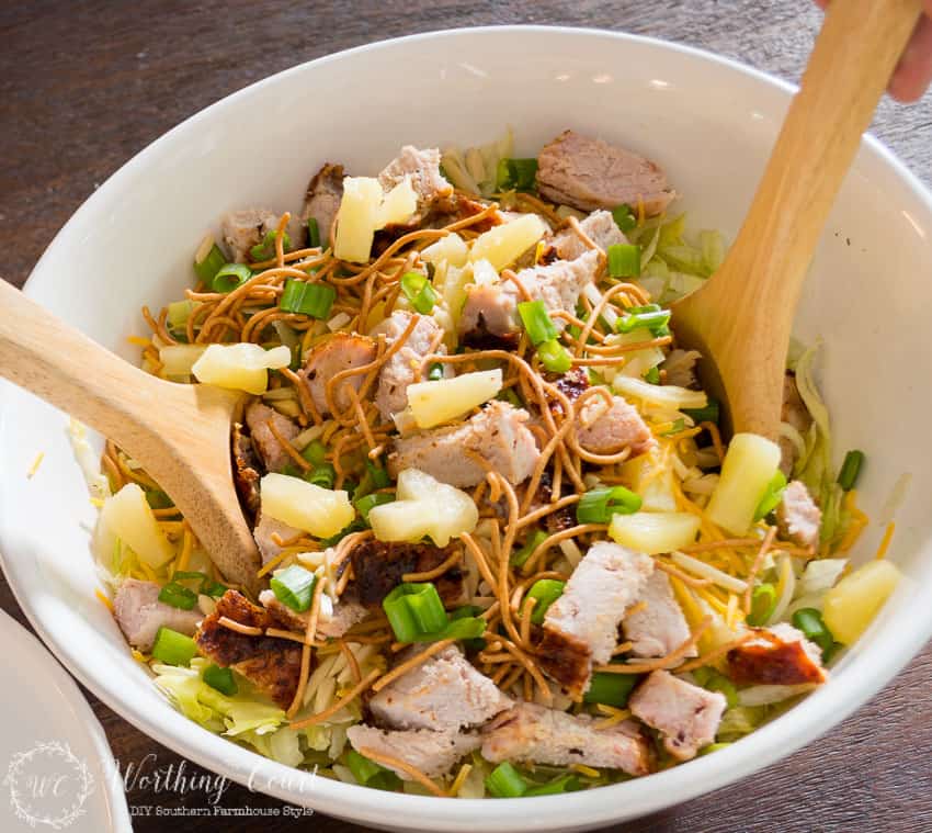 The salad in a white bowl with wooden salad servers in it to.