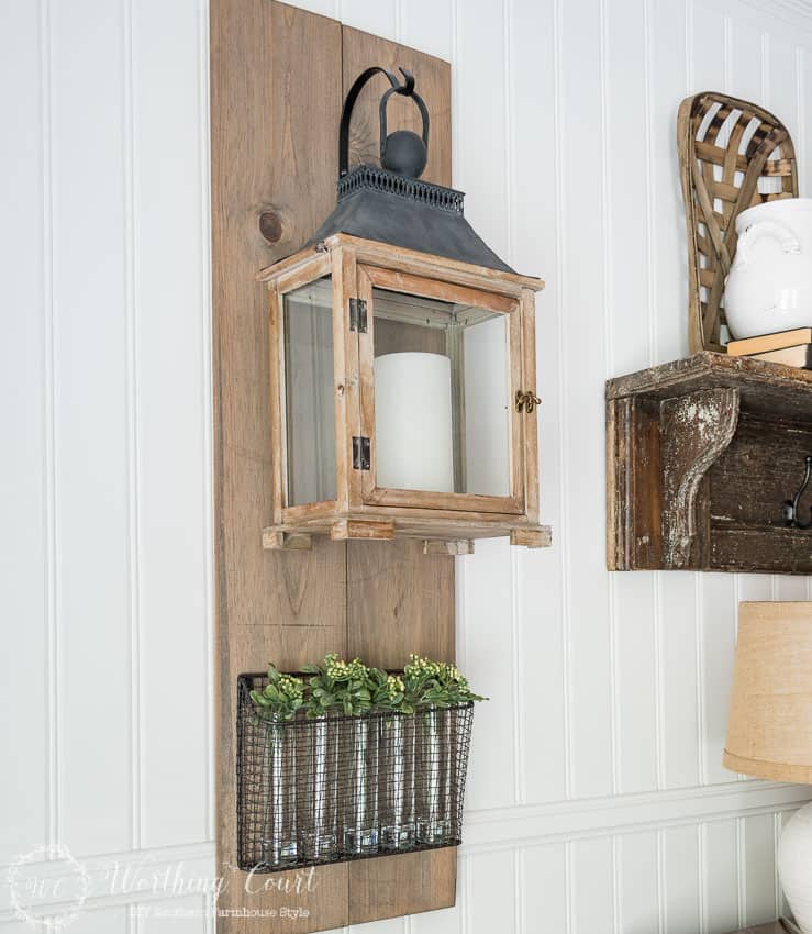 Farmhouse style lantern hanging from a diy wood plaque on the wall with a metal rack below it.