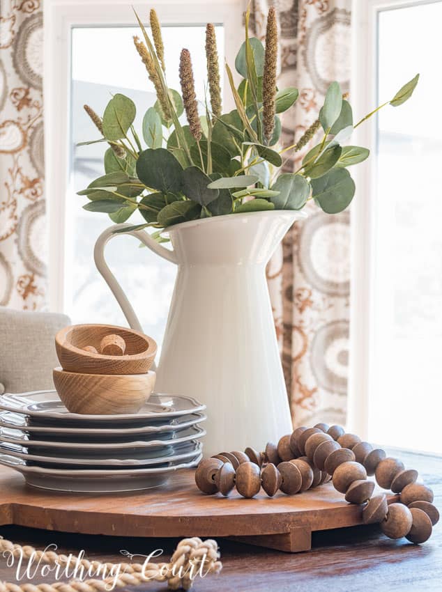 Fast and easy late summer to early fall farmhouse centerpiece with a white pitcher filled with greenery and wooden beads on the tray.